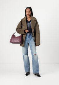 Abrigo sobre tamaño en verde oliva, blusa de punto azul marino, pantalones de mezclilla de tiro alto en azul claro con rotos, y un bolso de cuero burdeos. Zapatos negros de punta.