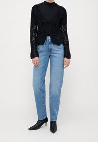 Černý pletený kardigan s otevřeným pletením, dlouhými rukávy a zavázáním. V kombinaci se světle modrými rovnými džíny a černými lodičkami se špičatou špičkou.