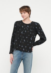 Svart langermet bluse med blå blomsterprint, rund hals, samlet detalj ved bysten, og litt puffede ermer. Lett stoffkvalitet.