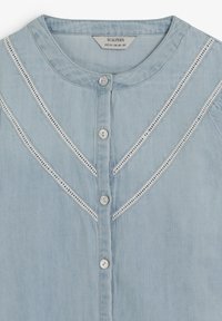 Camisa de mezclilla azul claro con cuello redondo, con detalles bordados en blanco y cierre de botones al frente. Tela suave y texturizada.