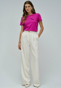 Camiseta de algodón fucsia con detalle de lazo, combinada con pantalones de tiro alto color crema que cuentan con bolsillos laterales y cierre de botones.