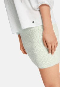 Hellgrüner, gestrickter Minirock aus strukturiertem Material, kombiniert mit einem weißen, locker sitzenden Oberteil mit Reißverschluss und abgerundetem Saum.