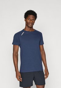 Jūras zila sporta T-krekls ar īsām piedurknēm, apaļu kakla izgriezumu un kontrastējošu šuvju. Uz kreisās pleca daļas ir logotipa detaļa.