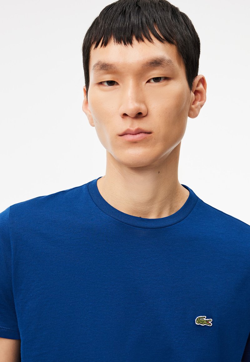 Royalblaue Baumwoll-T-Shirt mit Rundhalsausschnitt und kurzen Ärmeln, versehen mit einem kleinen gestickten Krokodil-Logo auf der Brust.
