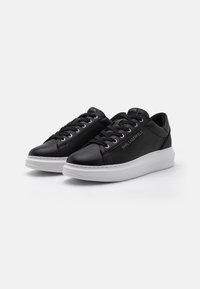 Black leather sneakers with white rubber soles, round toes, lace-up design, and subtle branding on the side and tongue. Smooth texture.