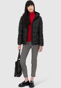 Giacca puffer nera con cappuccio, dolcevita rossa, pantaloni a fantasia bianco e nero, borsa nera e scarpe nere con fibbie. Texture lisce.