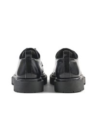 Scarpe in pelle lucida nera con suola in gomma spessa, caratterizzate da una finitura liscia e da un tassello sul retro, viste da dietro.