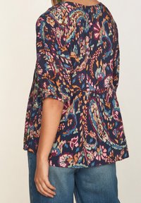 Blouse à motifs floraux avec manches bouffantes. Couleurs comprenant bleu marine, rose, orange et sarcelle. Tissu léger avec une coupe taille peplum.