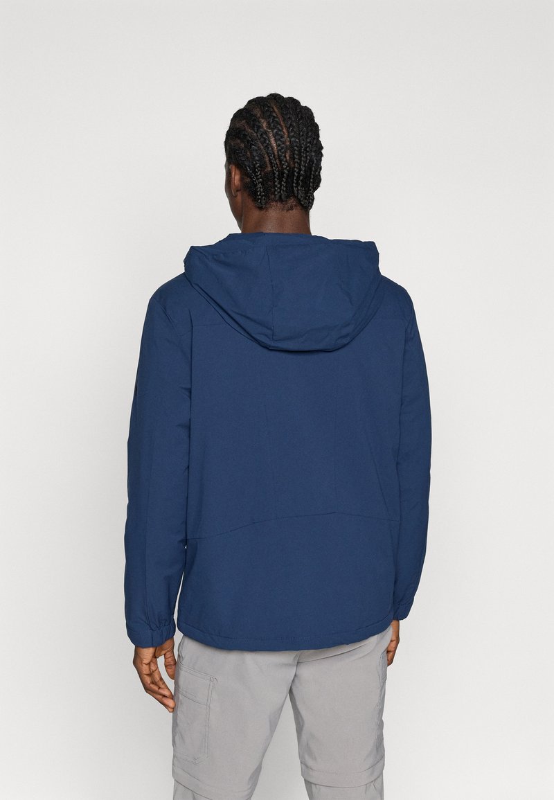 Chaqueta ligera de color azul marino con capucha, puños elásticos y ventilación en la espalda. Tejido suave con mínimos detalles de costura.