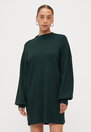 Mørkegrønn strikket kjole med høy hals, voluminøse ermer og ribbede mansjetter. Stoffet ser mykt ut med en jevn tekstur.