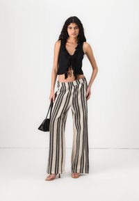 Black ruffled crop top with a tie front, paired with high-waisted, wide-leg pants featuring vertical black and beige stripes and a textured finish.