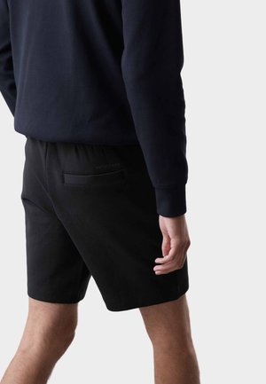 Pantalones cortos negros con cintura elástica y un bolsillo trasero, hechos de tela suave, combinados con una camiseta de manga larga oscura.
