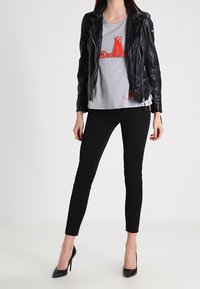 Sort læder bikerjakke over en grå t-shirt med rød tekst, parret med sorte leggings og sorte højhælede sko.