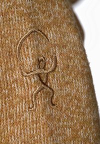 Stickad tröja i en varm gyllene brun med texturerat mönster. Har en framträdande mörkgul broderad figur som lyfter en cirkel.
