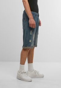 Shorts en jean bleu délavé avec des patchs usés et des ourlets roulés. Associés à des baskets blanches et des chaussettes mi-mollet. Design simple, coupe décontractée.