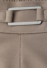 Beżowy materiał z pionowym szwem i prostokątnym, srebrnym metalowym klamrą przymocowaną do materiałowej pętli.