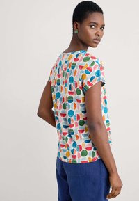 Short-sleeve top in light fabric, features a multicolored geometric pattern of circles and stripes on a white background.