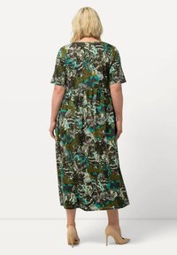 Maxikleid mit floralem und abstraktem Muster in Grün, Braun und Türkis. Kurze Ärmel. Ausgestellter Rock. Getragen mit beigen High Heels.