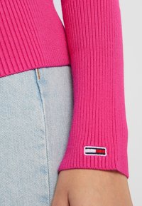 Enganliegendes, geripptes Sweatshirt in leuchtendem Pink, mit einem Tommy Hilfiger-Logo-Patch am Bündchen. Passt gut zu hellblauen Jeans.