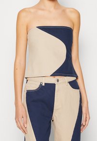 Top senza spalline beige e blu navy, caratterizzato da un design a blocchi di colore curvato con cuciture pulite. Abbinato a pantaloni a vita alta coordinati con blocchi di colore.
