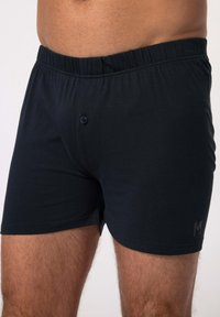 Tummansinisen puuvillan bokserishortsit, joissa on joustava vyötärö, yhdessä nappikiinnityksessä ja pieni logo helman kohdalla. Sujuva pinta.