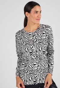 Cardigan con stampa zebra in bianco e nero, caratterizzato da scollatura tonda, chiusura con bottoni e maniche lunghe. Tessuto morbido e design aderente.