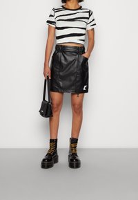 Svart läderkjol med samlade sidor och dragkedjedetalj, tillsammans med en svart och vit randig cropped topp och svarta platå lace-up stövlar.