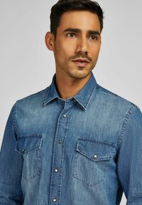 Jeanshemd in Hellblau mit Knopfleiste, spitzem Kragen und zwei Brusttaschen. Mit silbernen Druckknöpfen und einem strukturierten Stoff.