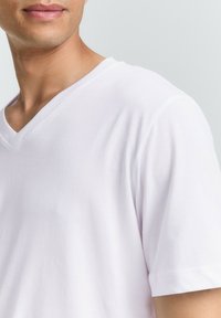 Weißes Baumwoll-V-Ausschnitt-T-Shirt mit kurzen Ärmeln, das eine glatte Textur und einen schlanken Schnitt aufweist, wobei der Hals- und Schulterbereich sichtbar ist.