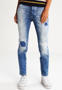 Vaqueros de color azul claro, hechos de denim, que presentan detalles desgastados con parches visibles, un ajuste slim y una cinturilla elástica.
