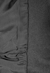 Gros plan de tissus tissés noirs et gris avec une texture visible et des plis sur le côté gauche, contre un tissu lisse sur le côté droit.