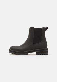 Botas negras hasta el tobillo con un exterior suave similar al cuero, paneles laterales elásticos y una suela de goma texturizada para mayor tracción. Diseño de puntera redondeada.