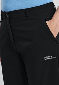 Zwarte softshell broek met een ritszak, logo op de bovenbeen en een zachte, licht elastische stof.