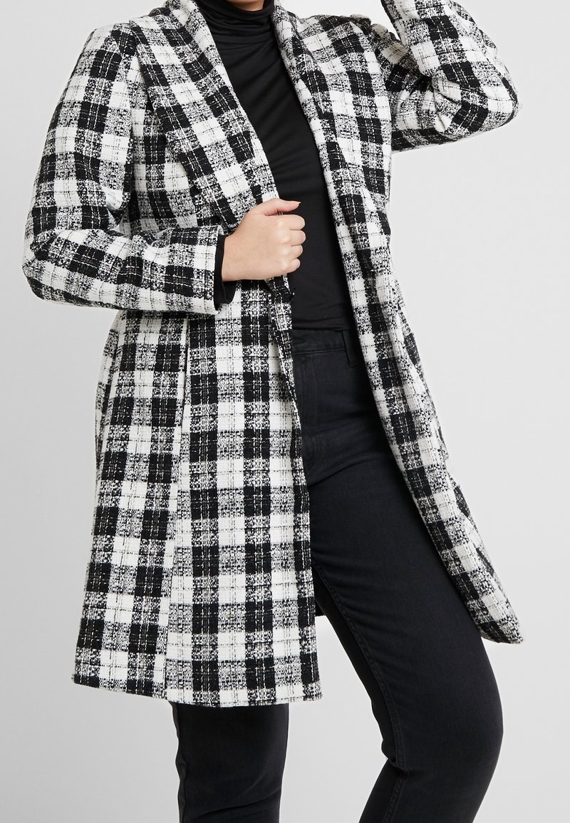 Abrigo de lana en blanco y negro a cuadros, con manga larga, frente abierto y diseño hasta la rodilla. TejidoTexturado con un patrón de cuadros clásico.