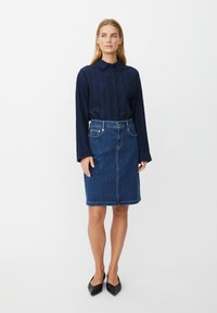 Chemise boutonnée à rayures navy associée à une jupe en denim longueur genou. La jupe présente une couture frontale, cinq poches et une fermeture à boutons.