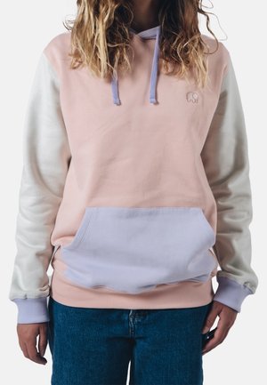 Person trägt einen pastellfarbenen Hoodie mit rosa Körper, weißen Ärmeln, lavendelfarbenen Bündchen und einer vorderen Kängurutasche, kombiniert mit blauen Jeans.