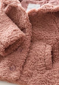 Różowa polarowa kurtka z fakturowaną powierzchnią, dwoma fioletowymi guzikami i detalem kieszeni. Wewnętrzna podszewka to gładki, wzorzysty materiał.