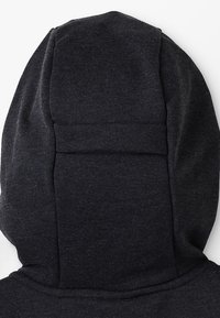 Mikina s kapucí v tmavě šedé tkanině s texturačním povrchem. Disponuje bezšvovým designem na zadní části kapuce pro čistý vzhled.