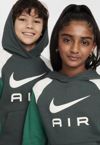 To barn iført matchende hettegensere. Hettegensrene er mørkegrønne med hvite detaljer og en stor hvit "AIR"-logo på fronten.