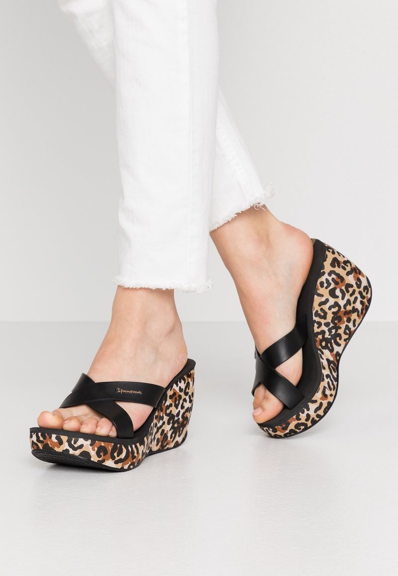 Sandales compensées à brides croisées noires avec une semelle plateforme imprimé léopard, présentant une texture lisse et une forme incurvée.