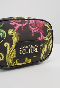 Petit sac noir Versace Jeans Couture avec des motifs baroques jaunes et roses et un patch logo sur le devant.