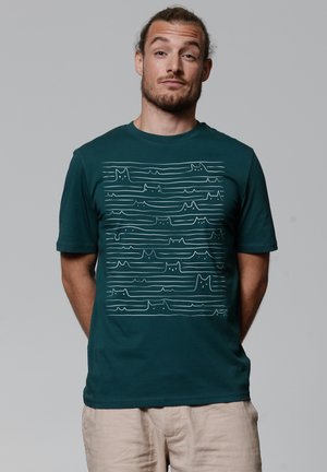 Groene katoenen t-shirt met een witte lijntekening van golven en kattenvormen. Korte mouwen en een ronde hals.