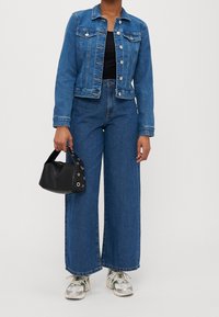 Jeansjacka i medelblå färg med framfickor och silverknappar. Vida jeans i matchande färg. Svart handväska med metallaccent och sneakers.