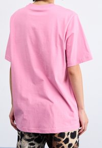 Růžové bavlněné tričko s krátkým rukávem a klasickým výstřihem, zobrazené zezadu, spárované se vzorovanými kalhotami s potiskem zvířat.