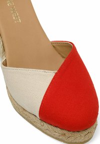 Espadrille compensée rouge et beige avec une tige en toile, bout rond et semelle en jute ; présente une couture marquée entre les couleurs.