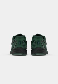 Une paire de chaussures de sport noir et vert foncé vues de l'arrière, présentant des superpositions en maille et en synthétique avec un amorti d'air visible dans le talon.