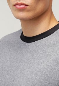 Chemise grise à manches courtes avec un col noir, fabriquée en tissu doux, présentant une texture lisse et un design simple.