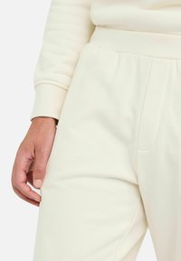 Pantalones de chándal color crema fabricados con una tela suave y con un acabado texturizado, que cuentan con una banda en la cintura y bolsillos laterales.