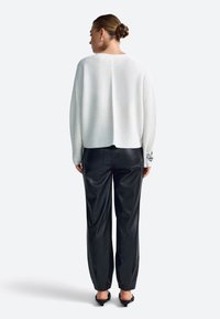 White textured sweater with a rounded back hem, paired with black faux leather trousers and low-heel shoes. Silver accent on sleeve.