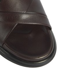 Bruine leren slip-on sandaal met kruisbandontwerp; gladde textuur; ronde neus en platte rubberen zool. Geometrische silhouet.